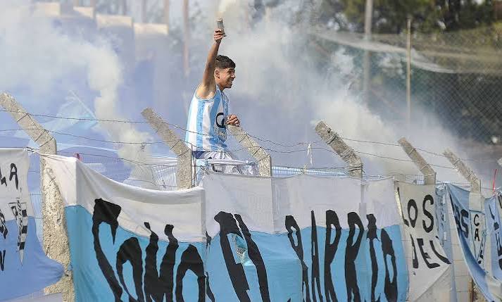 Hincha de Racing de Córdoba en la tribuna entre humo y banderas celestes y blancas